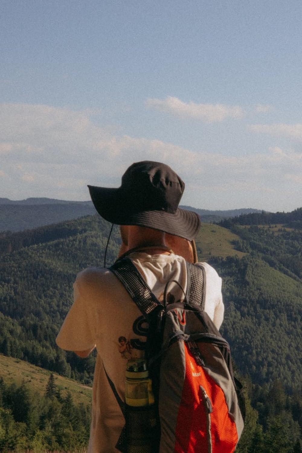 man_in_hat_and_with_backpack_standing_with_hills_b